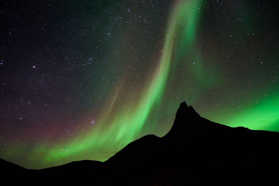 Green northern lights sweeping above a dark mountain ridge at night.